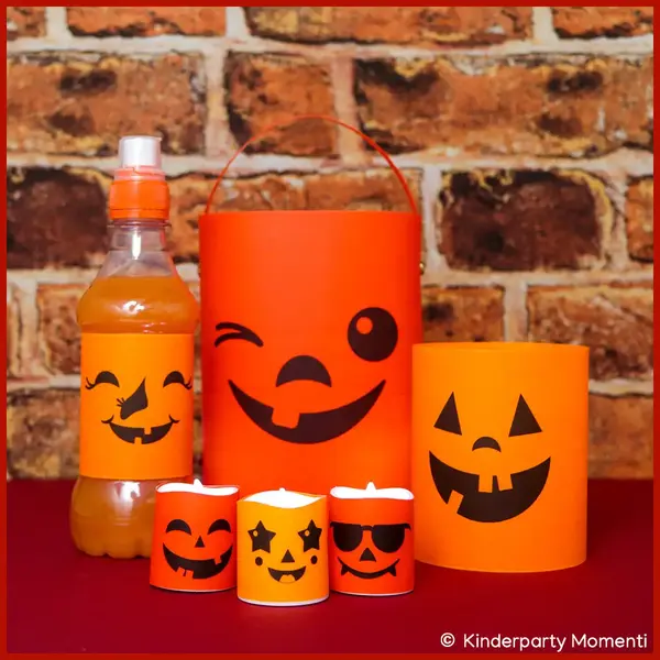 Deko für Halloween selber basteln mit Kürbisgesichter Vorlagen Orangefarbene Halloween-Dekorationen mit schwarzen lachenden Gesichtern, darunter eine Flasche, eine Laterne, ein Windlicht und drei kleine Teelichtkerzen vor Ziegelsteinwand