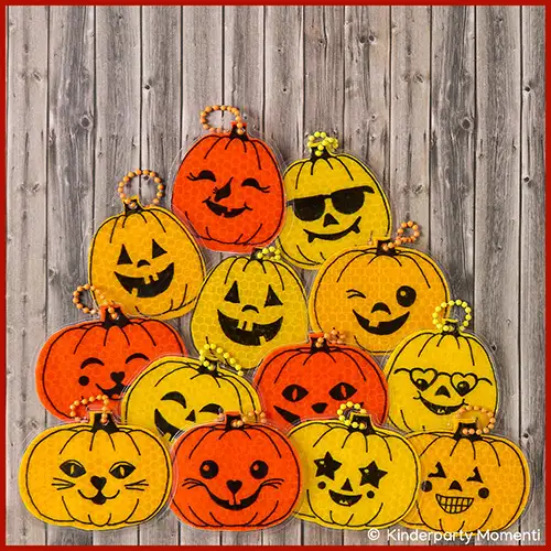 Kleine gelbe und orangene, aus Reflektorband gebastelte, Anhänger mit fröhlichen Kürbisgesichtern.