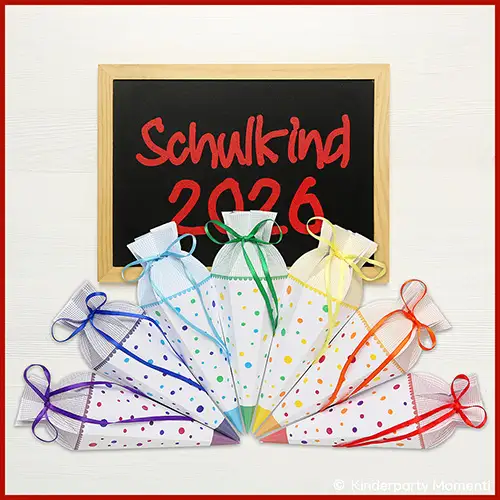 Sieben kleine Schultüten mit bunten Punkten und farblich passenden Schleifen vor einer Tafel mit roter Schrift 'Schulkind 2026'