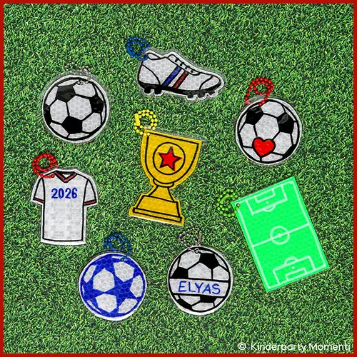 Reflektierende Anhänger in Form von Fußbällen, Fußballschuh, Trikot mit '2026', Pokal, Fußballfeld und Fußball mit dem Namen 'ELYAS' auf grünem Rasen