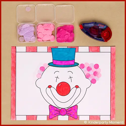 Bastelvorlage mit Clown Kopf, roter Nase, blauem Zylinder, pinker Fliege und rosa Papierscheiben als Haare, daneben drei Behälter mit rosa Papierscheiben und ein Kleberoller