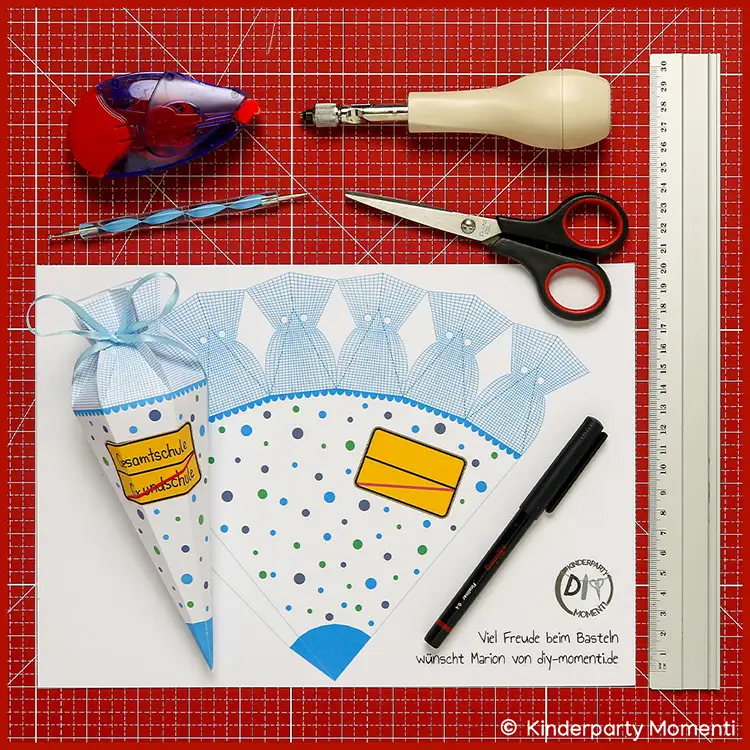 Bastelmaterial & Druckvorlage für kleine Schultüte mit Ortsschild Bastelvorlage für eine Schultüte mit blauem Schleifenband, Schere, Lineal, Kleberoller, Stift und Werkzeug auf roter Bastelmatte