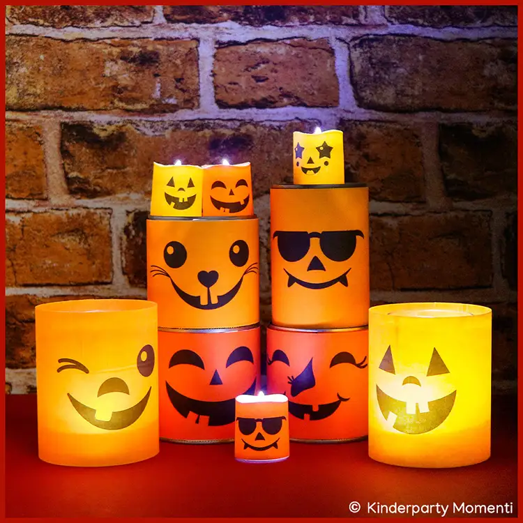 Leuchtende Halloween-Windlichter aus Papier mit verschiedenen lachenden Gesichtern, vor einer Ziegelsteinwand auf rotem Untergrund