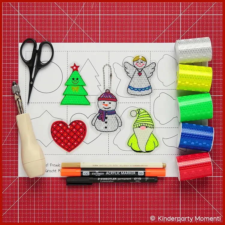 Druckvorlagen für Weihnachtsanhänger Bastelvorlage mit ausgeschnittenen Weihnachtsanhängern: Tannenbaum, Herz, Schneemann, Engel, Wichtel, daneben Schere, Stifte und reflektierende Klebebänder in verschiedenen Farben.