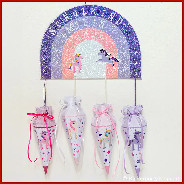 Regenbogen Deko mit kleinen Schultüten An einem Regenbogen aus Papier hängen vier kleine Schultüten mit Einhorn Aufklebern.
