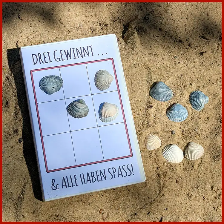 Reisespiel mit Muscheln Ein Tic-Tac-Toe-Spiel mit Muscheln liegt am Strand im Sand.