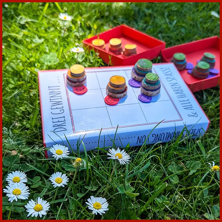 Kleines Spiel zum Mitnehmen in den Park Ein Tic-Tac-Toe-Spiel mit Schnecken Spielsteinen liegt auf einer Wiese.