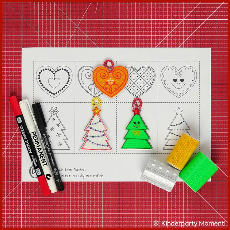 Reflektoren Weihnachtsanhänger selber machen Bastelvorlage mit vier Herz- und vier Tannenbaumformen, zwei bunte Tannenbaumanhänger, drei bunte Klebefolien und drei Marker auf roter Bastelmatte